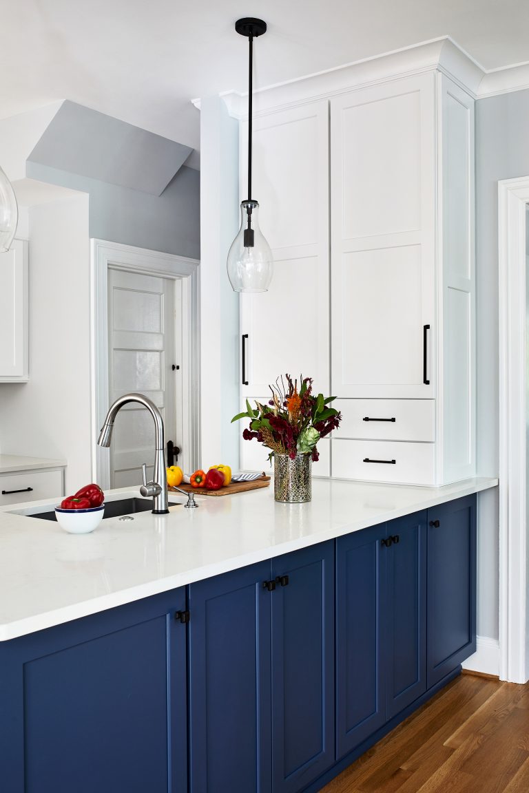 blue kitchen cabinets with black knobs, white marble counter tops and white cabinets with pull handles