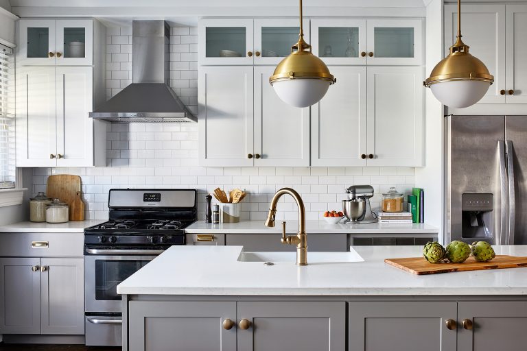 white marble top kitchen island with gold faucets and white opal brass two-light pendant with frosted glass above kitchen island