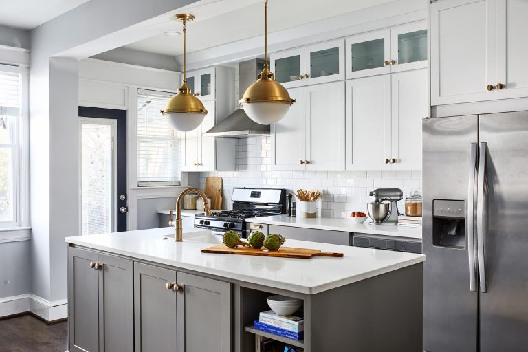 grey cabinetry on the island with white tall cabinets and gold knobs with stainless steel appliances